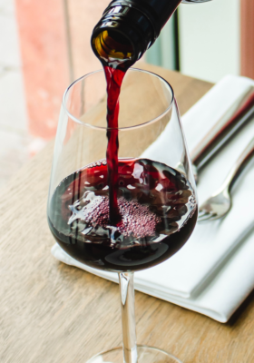 A table setting featuring a large stemmed wine glass being filled with delicious red wine